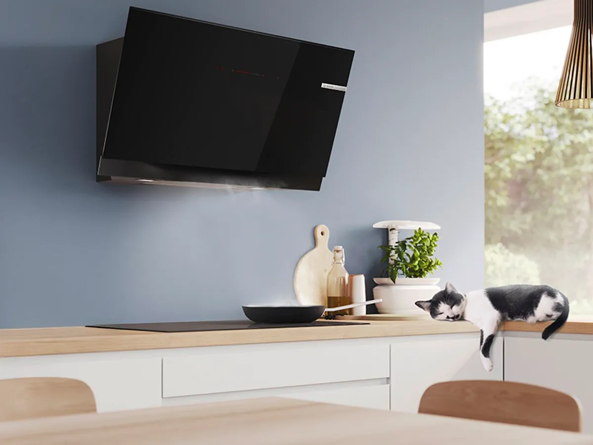 Gian bếp căn hộ với máy hút mùi Bosch kính đen áp tường phía trên bếp từ, chảo trên mặt bếp, kệ gỗ và cây xanh