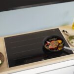Chảo áp chảo thịt và rau củ trên bếp từ Bosch lắp âm mặt bếp gỗ, bên cạnh chai dầu ăn