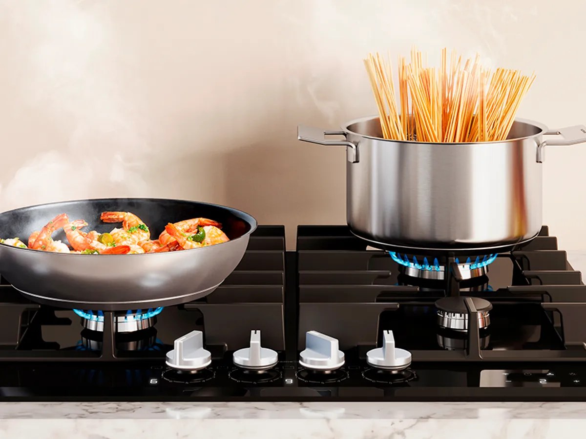 Bếp gas âm Bosch mặt kính đen với chảo xào tôm và nồi mì trên kiềng, đầu đốt đang cháy lửa xanh